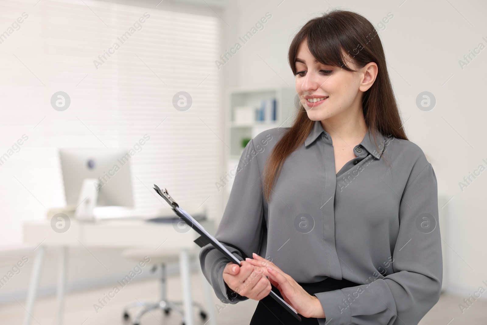 Photo of Portrait of smiling secretary with clipboard in office. Space for text