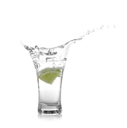 Splashing Mexican Tequila in shot glass with lime slice isolated on white