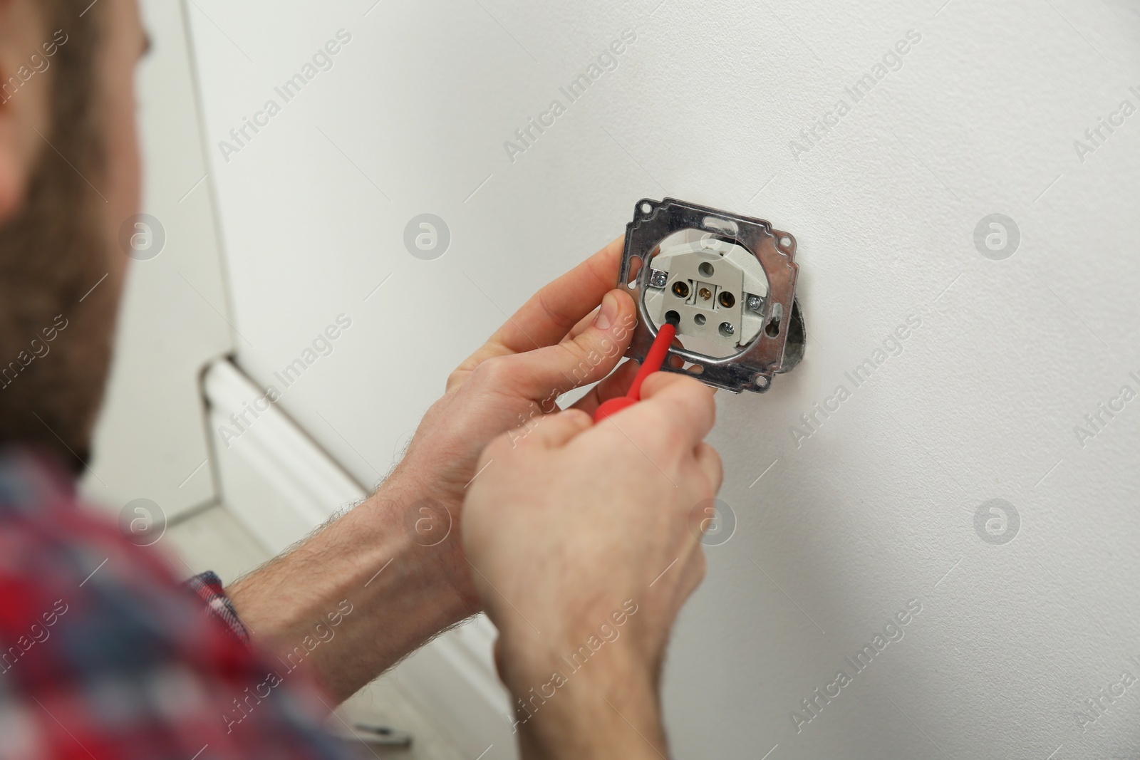 Photo of Electrician with screwdriver repairing power socket indoors, closeup