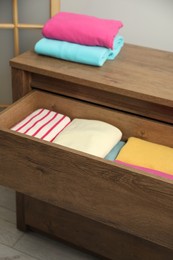 Photo of Wooden chest of drawers with different folded clothes indoors, closeup