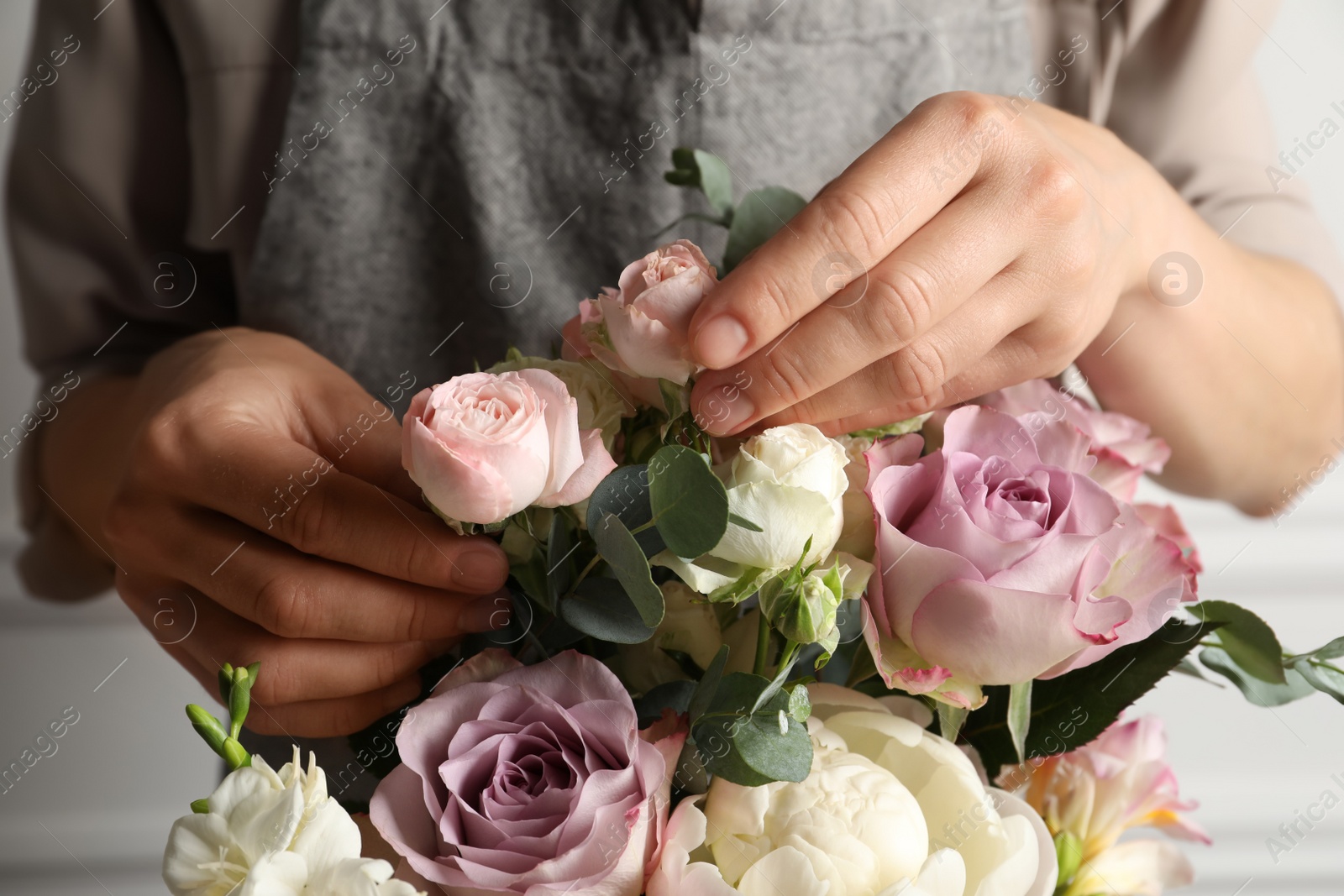Photo of Florist creating beautiful bouquet with roses indoors, closeup