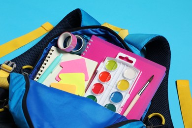 Backpack with school stationery on light blue background, closeup