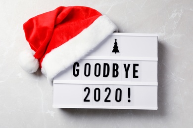 Lightbox with text Bye Bye 2020! and Santa hat on light grey background, flat lay