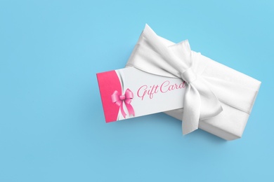 Gift card and present on light blue background, top view. Space for text