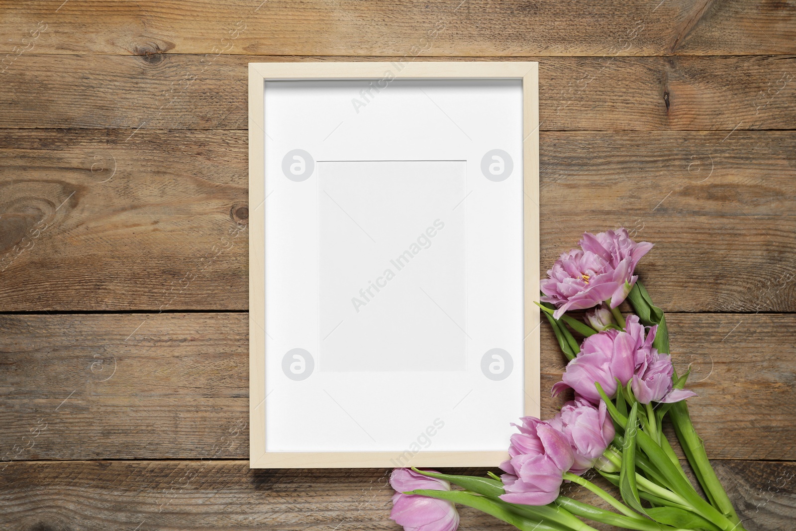 Photo of Empty photo frame and beautiful flowers on wooden table, flat lay. Space for design