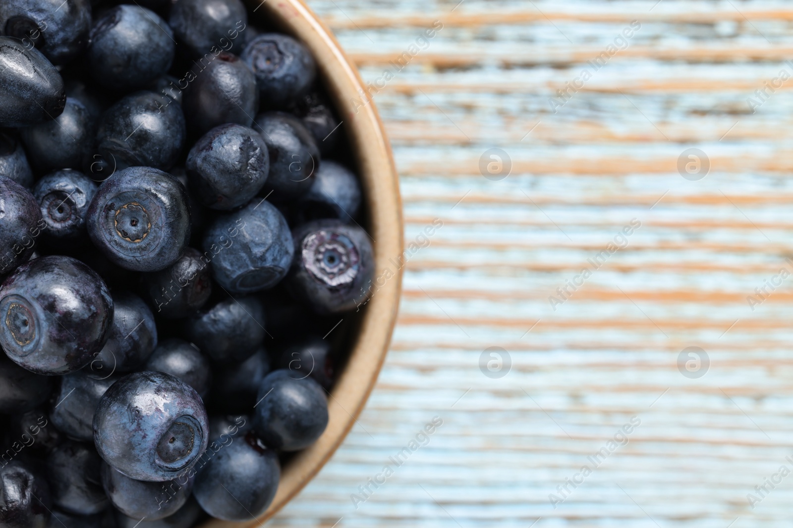 Photo of Tasty fresh bilberries in bowl on old light blue wooden table, top view. Space for text