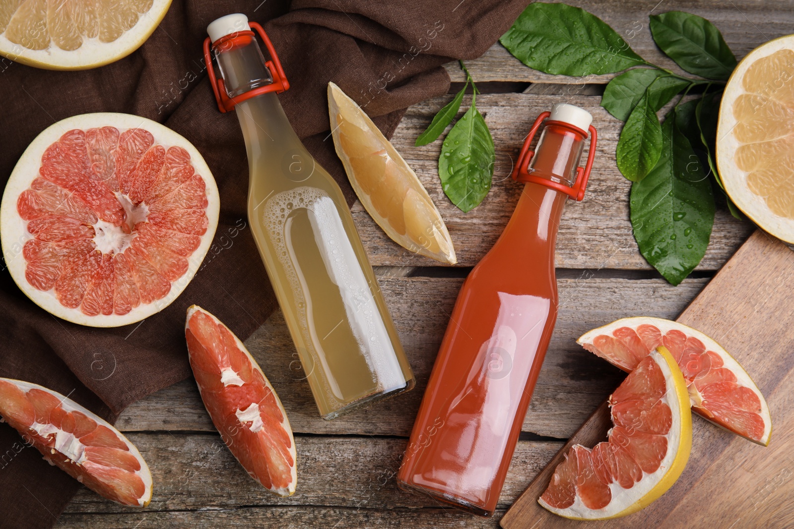 Photo of Glass bottles of different pomelo juices and fruits on wooden table, flat lay