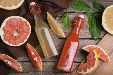 Glass bottles of different pomelo juices and fruits on wooden table, flat lay