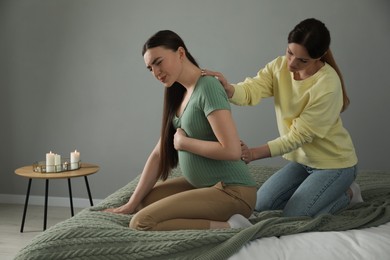 Doula massaging pregnant woman in bedroom. Preparation for child birth