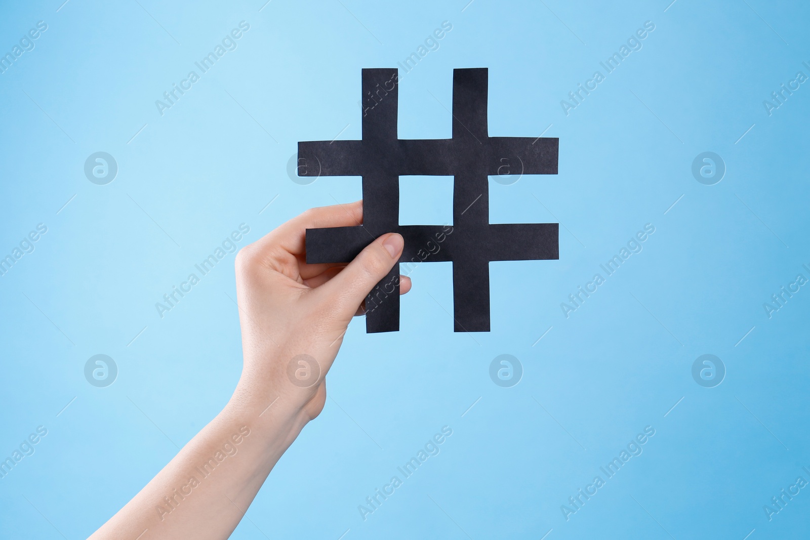 Photo of Woman holding black paper cutout symbol of hashtag on turquoise background, closeup