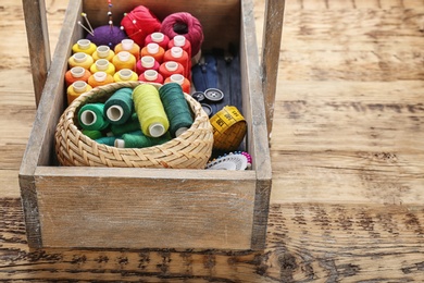 Box with color sewing threads on wooden background