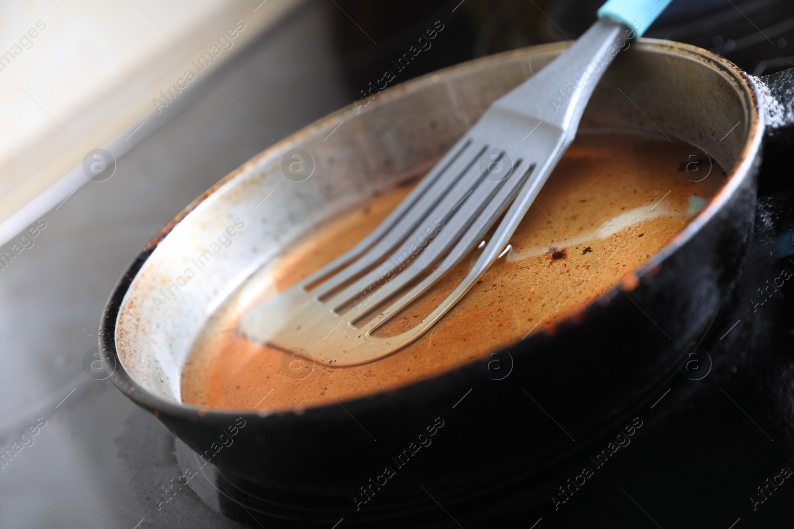 Photo of Frying pan with spatula and used cooking oil on stove, closeup