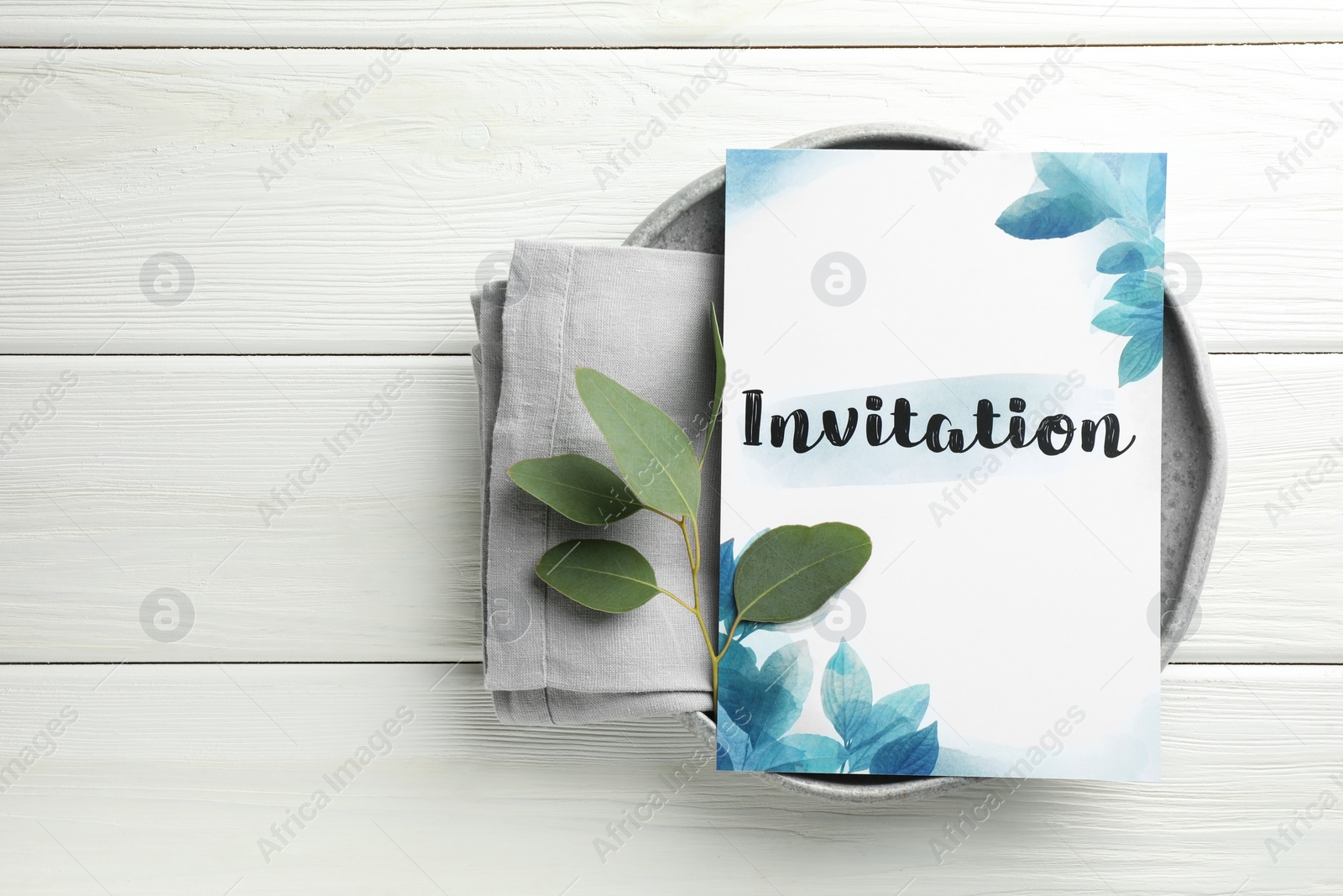 Photo of Card with word Invitation, towel and green leaves on white wooden table, top view. Space for text