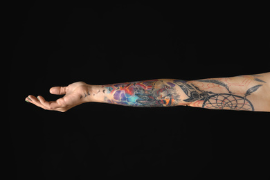 Photo of Woman with colorful tattoos on arm against black background, closeup