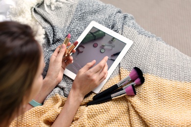 Photo of Young woman with makeup products using tablet on bed. Beauty blogger