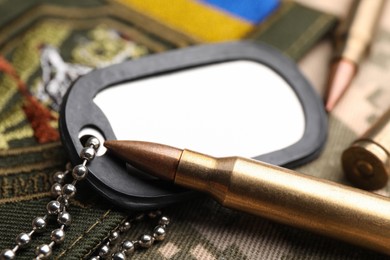 Photo of Bullets, military ID tag and Ukrainian patch on pixel camouflage, closeup