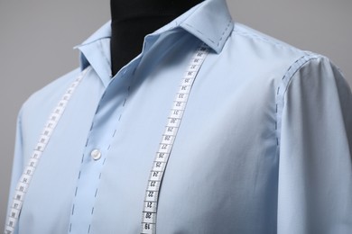 Photo of Semi-ready shirt with tailor's measuring tape on mannequin against grey background, closeup