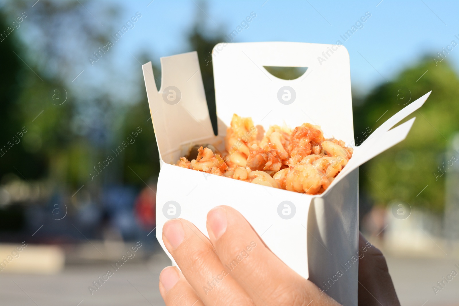 Photo of Woman holding paper box with takeaway noodles outdoors, closeup and space for text. Street food