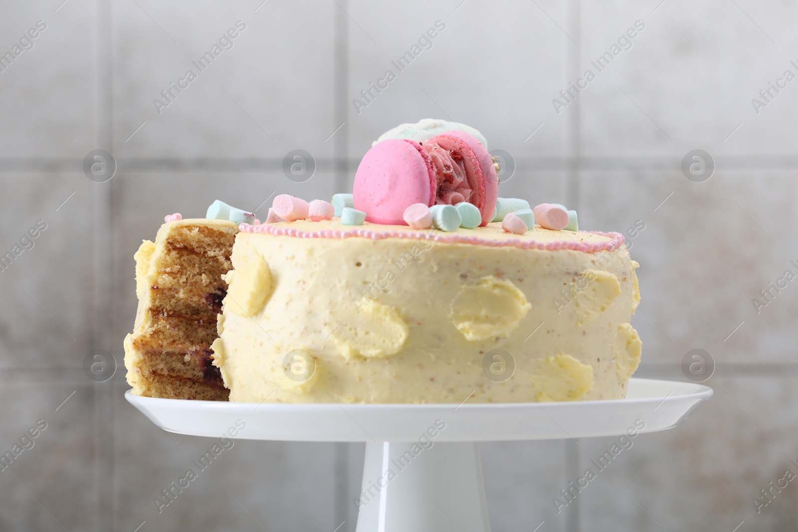 Photo of Delicious cake decorated with macarons and marshmallows against light tiled background, closeup