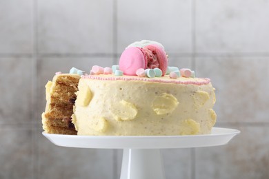 Delicious cake decorated with macarons and marshmallows against light tiled background, closeup