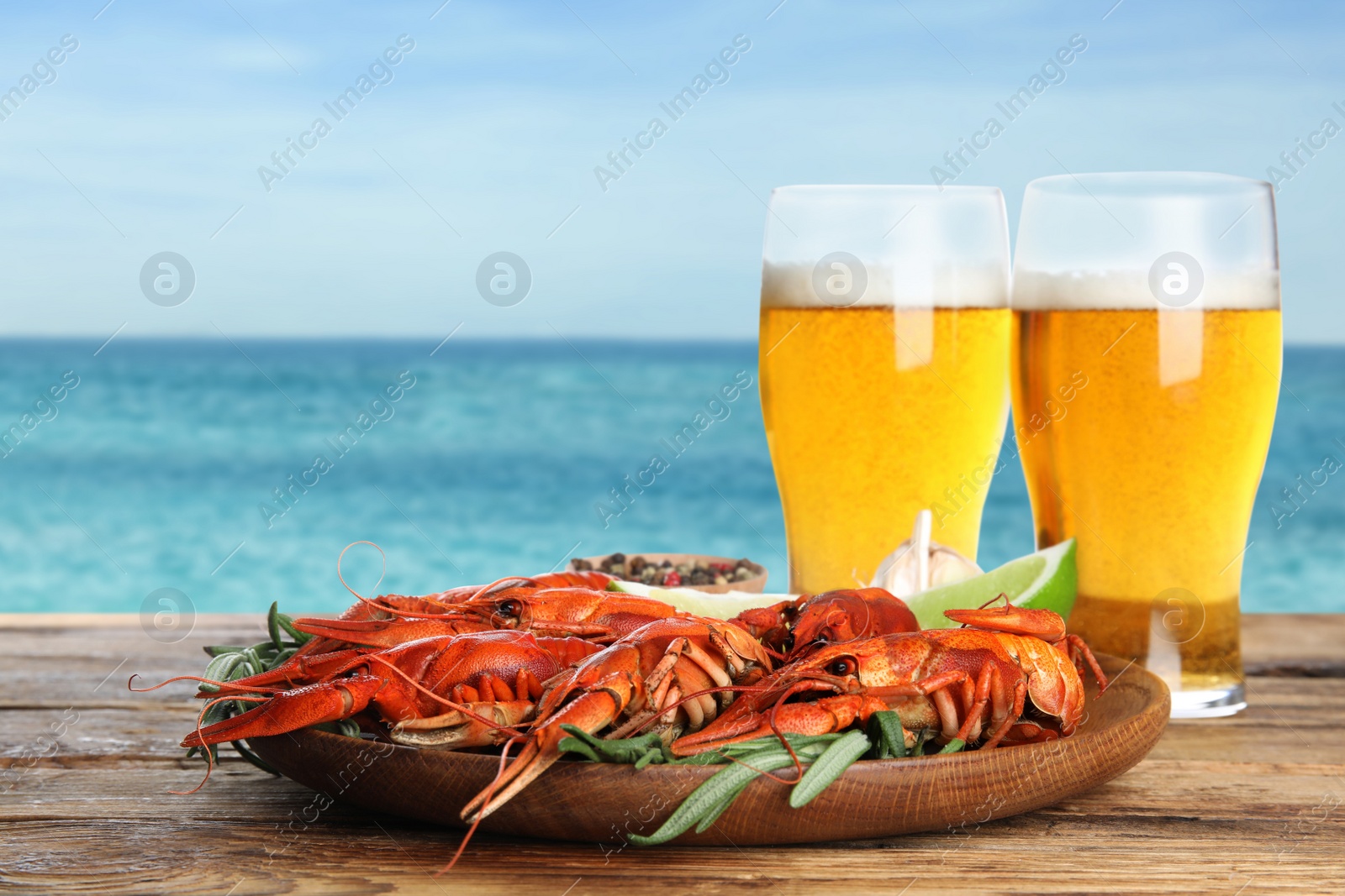 Image of Cooked crayfishes served with beer on wooden table near sea