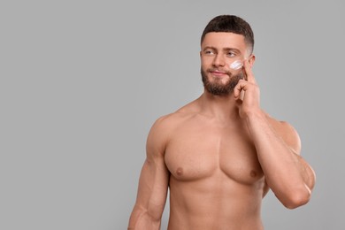 Handsome man applying cream onto his face on light grey background, space for text