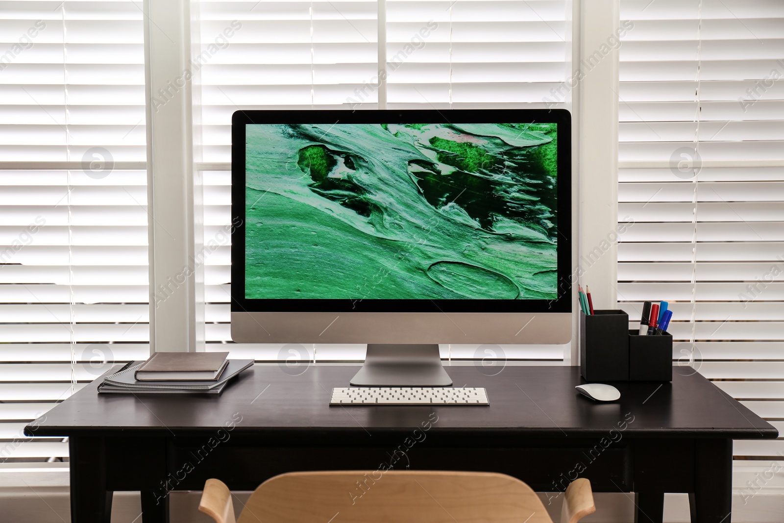 Photo of Comfortable workplace near window with white horizontal blinds in room