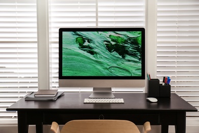 Photo of Comfortable workplace near window with white horizontal blinds in room