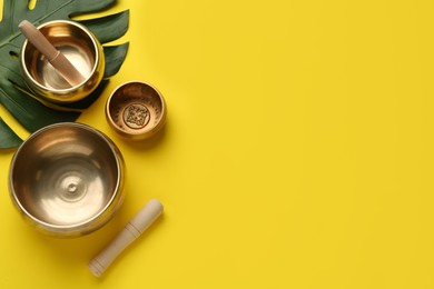 Photo of Golden singing bowls, mallets and monstera leaf on yellow background, flat lay. Space for text