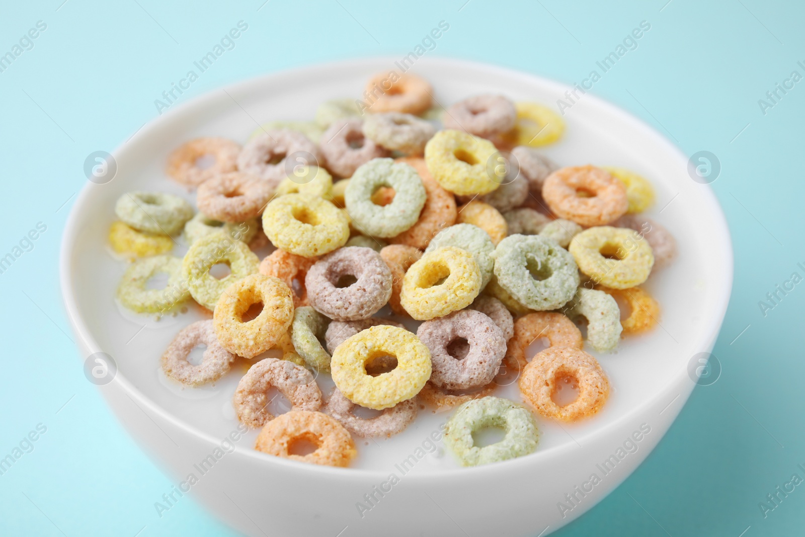 Photo of Tasty colorful cereal rings and milk in bowl on turquoise background, closeup