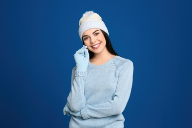 Photo of Young woman wearing warm sweater, gloves and hat on blue background. Winter season