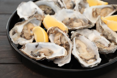 Fresh oysters with cut juicy lemon on plate, closeup