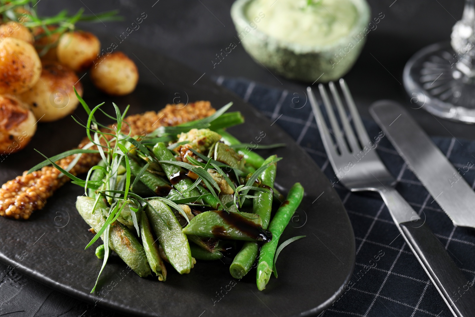 Photo of Delicious salad with tarragon, mustard and grilled potatoes served on black table, closeup
