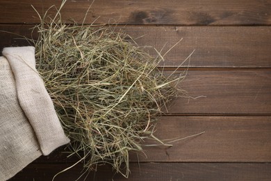 Photo of Dried hay in burlap sack on wooden table, top view. Space for text