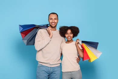 Happy African American couple with shopping bags on light blue background