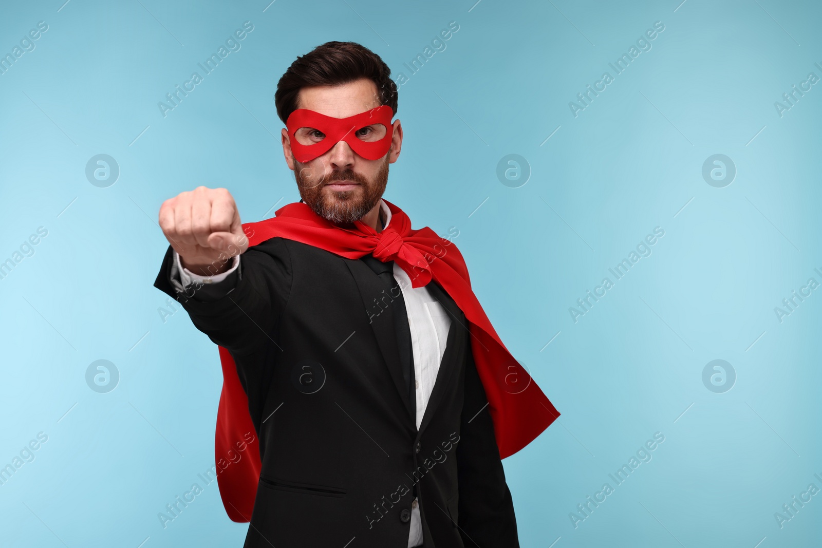 Photo of Businessman wearing red superhero cape and mask on light blue background