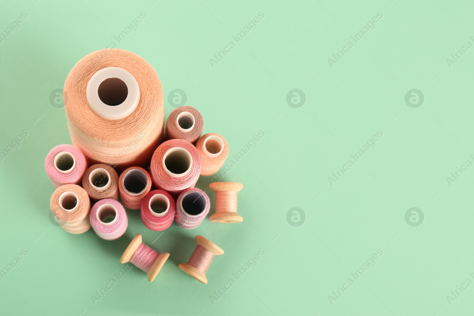 Photo of Different shades of pink sewing threads on turquoise background, flat lay. Space for text