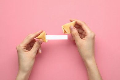 Photo of Woman holding tasty fortune cookie and paper with prediction on pink background, top view. Space for text