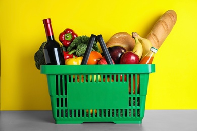 Photo of Shopping basket with grocery products on grey table against yellow background