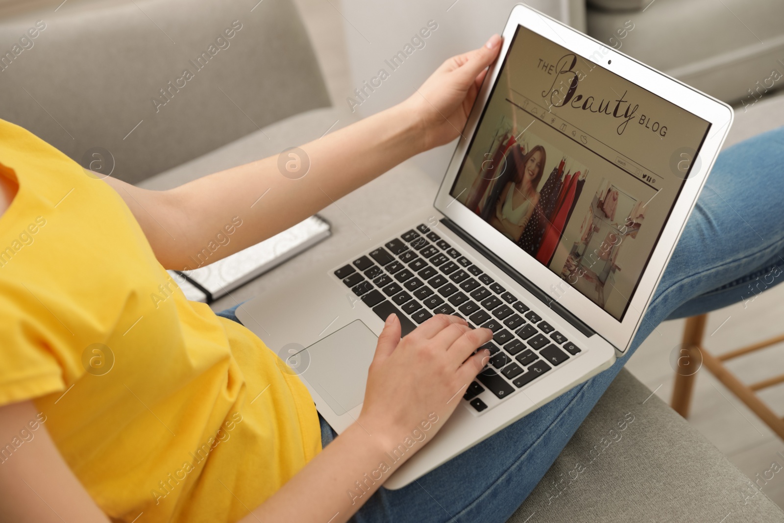 Photo of Woman holding laptop with open beauty blogger site on sofa, closeup