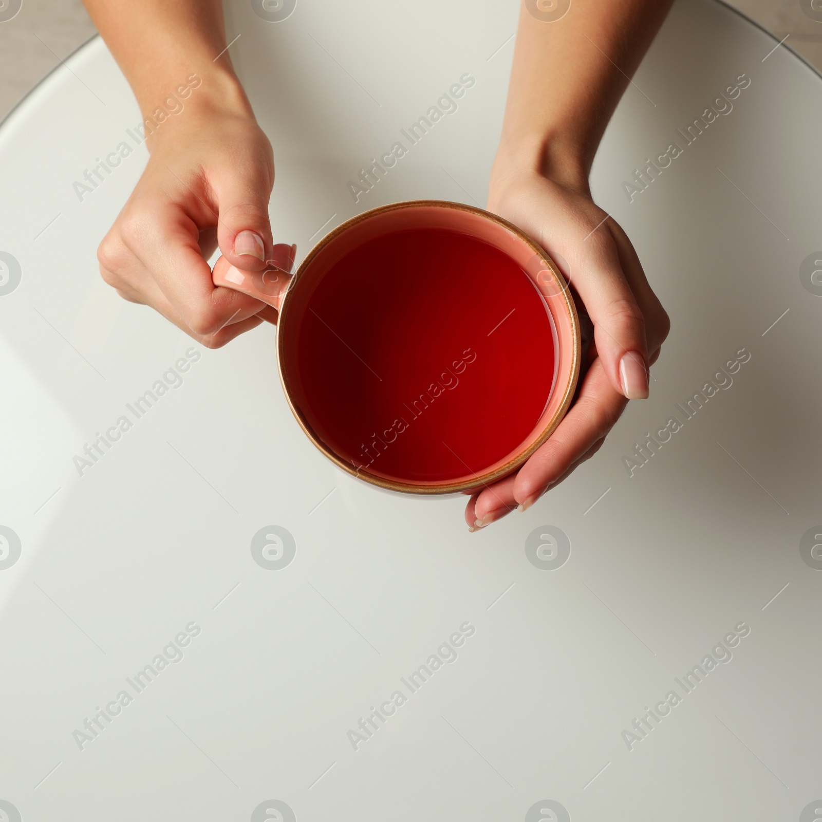 Photo of Woman with cup of black tea at white table indoors, top view