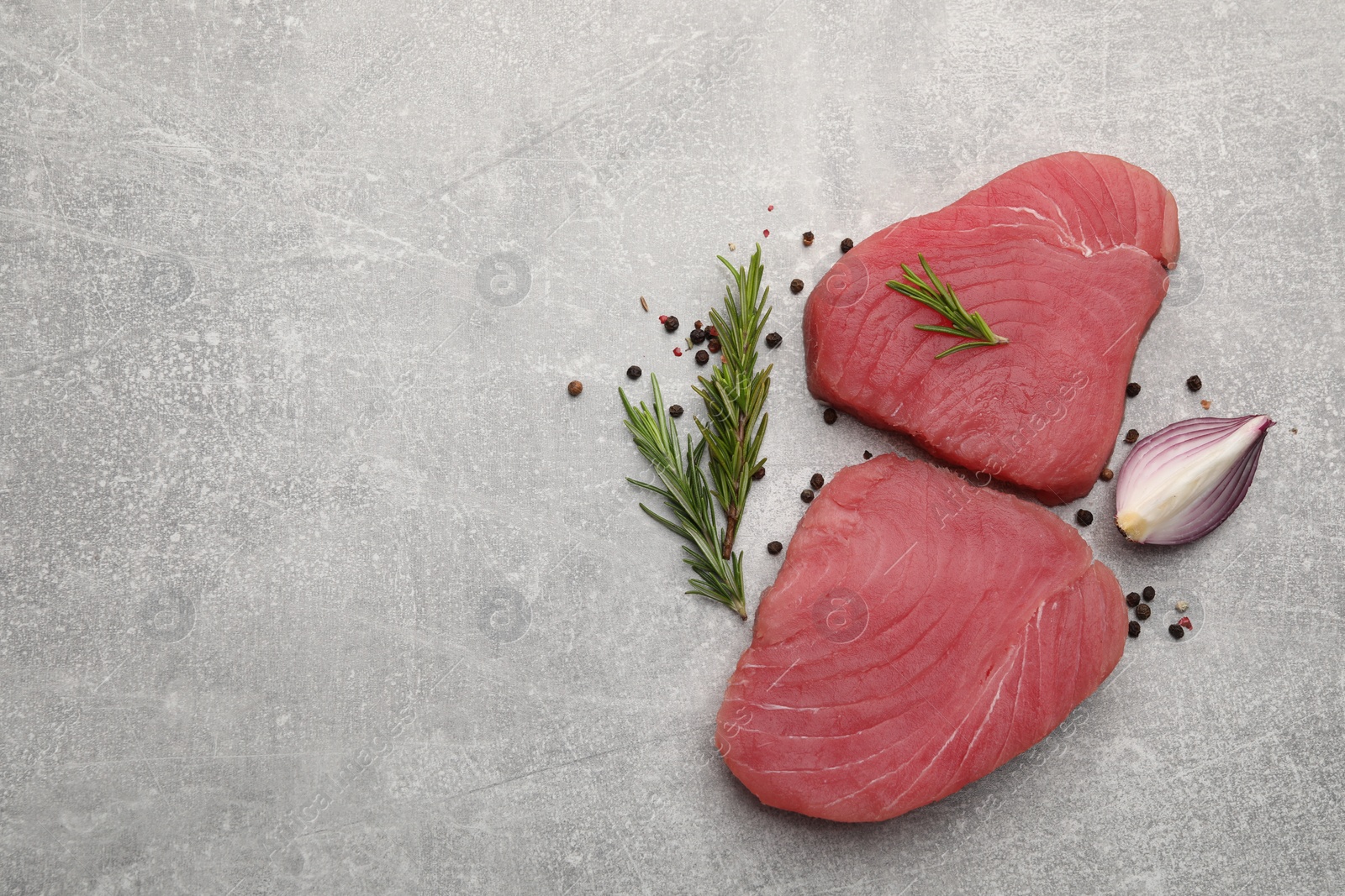 Photo of Fresh raw tuna fillets with rosemary and spices on light gray table, flat lay. Space for text