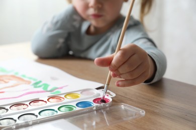 Little girl with brush drawing at wooden table indoors, selective focus. Child`s art