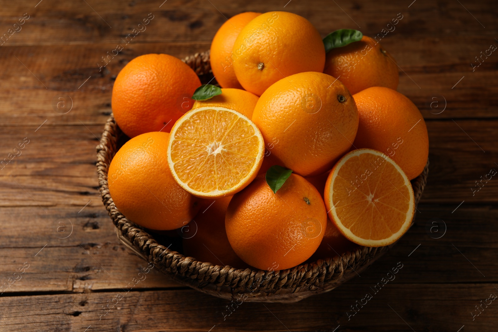 Photo of Many ripe oranges and green leaves on wooden table