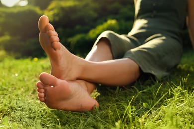 Woman sitting barefoot on green grass outdoors, closeup