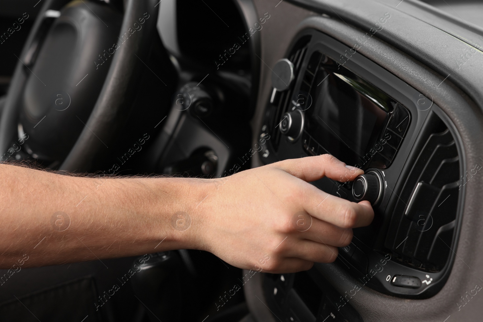 Photo of Listening to radio while driving. Man turning volume button on vehicle audio in car, closeup