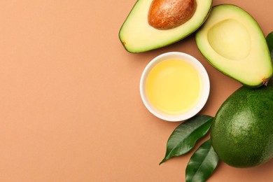 Cooking oil in bowl and fresh avocados on beige background, flat lay. Space for text
