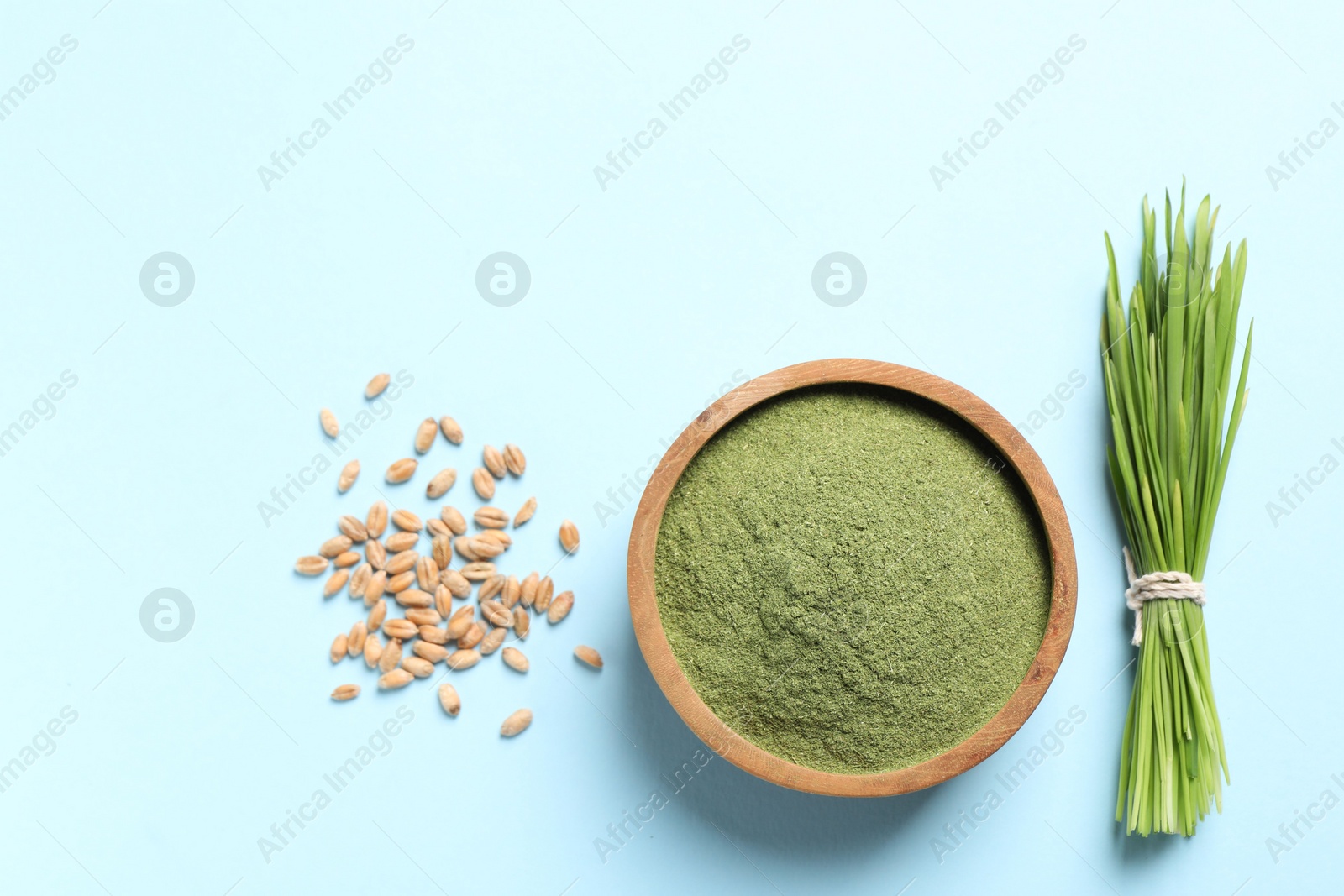 Photo of Wheat grass powder in bowl, seeds and fresh sprouts on light blue background, flat lay