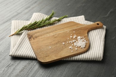 Photo of Wooden cutting board, kitchen towel, rosemary and salt on dark grey table