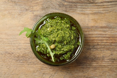 Photo of Bowl of tasty arugula pesto on wooden table, top view